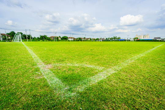 Corner of football field grass at stadium, blue sky background.