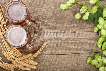 glass of foamy beer with hop cones and wheat on old wooden background. Top view with copy space for your text