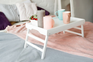 Breakfast in bed. Modern bedroom in pastel colors. Coffee and strawberries on small table decorated candles. Romantic concept and tendance between couples, close up side view