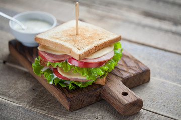 Close-up big sandwich with ham, cheese, tomatoes, salad and white sauce on toasted bread on a rustic wooden table