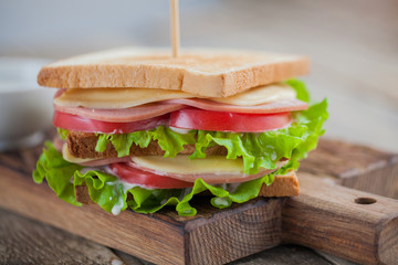 Close-up big sandwich with ham, cheese, tomatoes, salad and white sauce on toasted bread on a rustic wooden table