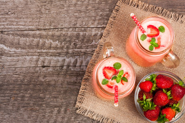 Glass of strawberry yogurt or smoothie with mint leaves on old wooden background with copy space for your text. Top view