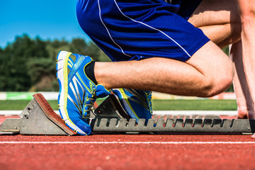 Runner before start signal on starting block of sprint track in sport stadium