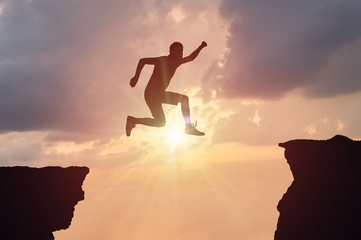 Silhouette of man jumping over a gap at sunset.
