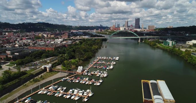 A high angle right moving aerial establishing shot of a marina on the Monongahela River with the Pittsburgh skyline in the distance.  	