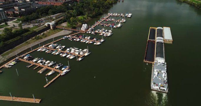 A cinematic high angle aerial flyover and tilt up shot of a marina and coal barge on the Monongahela River in Pittsburgh, PA.  	