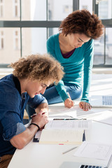Young creative student writing observations and ideas for an assignment while sitting at desk next...