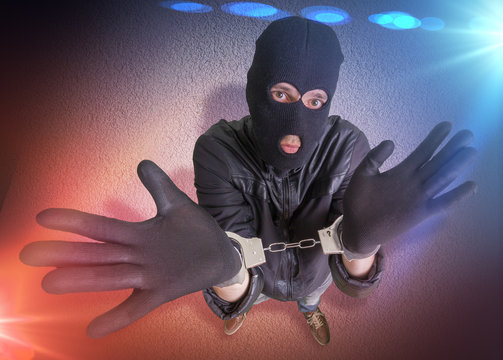 Thief or burglar with handcuffs is arrested. Police lights in background. View from above.
