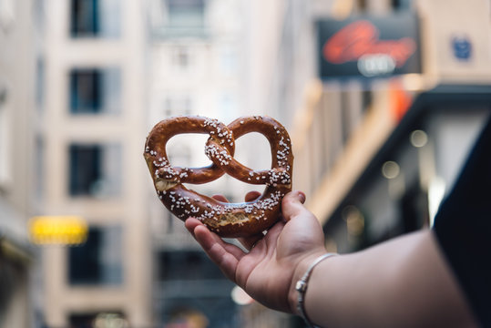 Woman Hand Holding A Pretzel Against Cityscape.