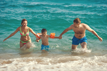 Family of three people getting out from the sea water. Front view.