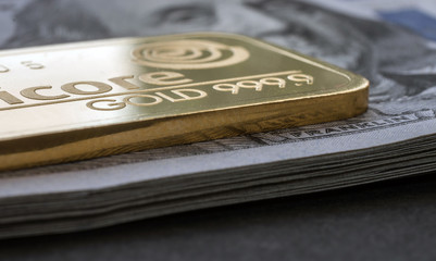 Minted gold bar lies on a stack of hundred-dollar bills. Selective focus.