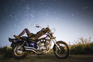 Fototapeta na wymiar Young beautiful biker woman with motorcycle under stars of Miky Way galaxy . Female biker at night