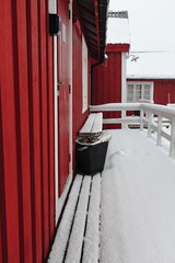 Tourist rorbuer-traditional seasonal cottages-gangplank and bench under snowfall. Hamnoy-Reine-Moskenesoya-Lofoten-Norway. 0384-2