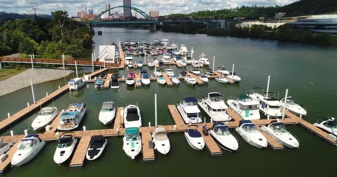A low angle forward moving aerial establishing shot of a boating marina on the Monongahela River with the Pittsburgh skyline in the distance.  	