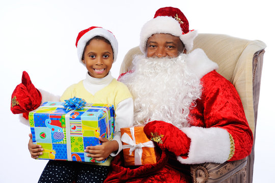 a black man, an African American in Santa Claus costume, sits in a chair. Child girl sitting on Santa's lap