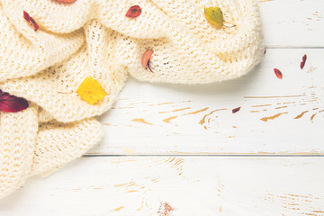 Knitted warm clothes with autumn leaves in an autumnal setting on a wooden table. Comfort, warmth, cozy.