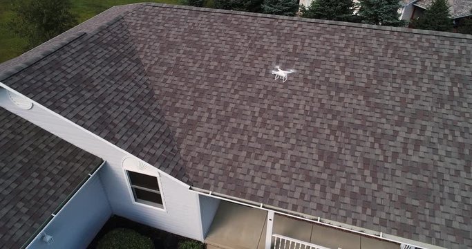 A high angle aerial view of a building inspector examining the roof of a residential home.  	