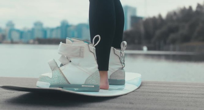 Young female in a swimsuit tightens wakeboard boots, prepares for a wakeboarding session. 4K UHD 60 FPS 
