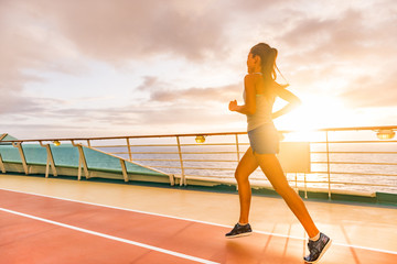 Fitness girl doing running cardio workout on cruise vacation. Fit woman jogging at sunset on run...