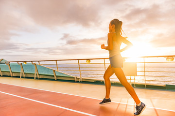 Naklejka premium Fitness girl doing running cardio workout on cruise vacation. Fit woman jogging at sunset on run lanes on deck of cruise ship during summer holidays. Active healthy lifestyle.
