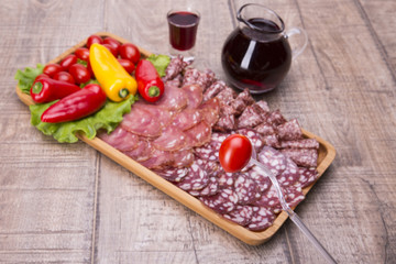 Set of meat delicatessen, tomatoes and peppers, wine on a wooden table.