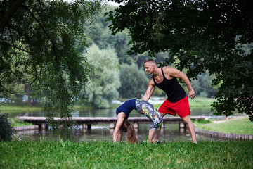 The male instructor in the park holds the girl by a back during the training.