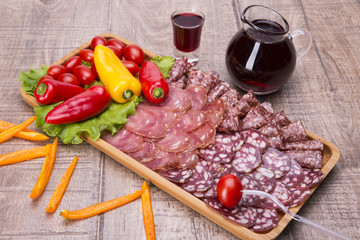 Set of meat delicatessen, tomatoes and peppers, wine on a wooden table.