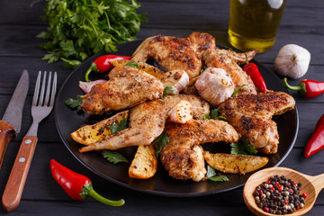 Grilled chicken wings on black plate decorated with garlic and spices. Cooking concept, meat dishes, homemade food