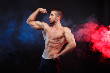 Strong young man bodybuilder demonstrating huge muscles on smoke background. Man with perfect abs, shoulders,biceps, triceps, chest. Sport, fitness, motivation concept