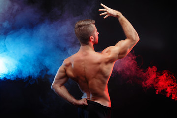 Bodybuilder man with perfect abs, shoulders,biceps, triceps and chest flexing his muscles, studio shoot, view from the back