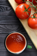 Tomato Juice in Green Enamel Mug on a Black Wooden Table with Fresh Branch of Tomatoes on a Wooden Cutting Board Top View. Background with a Blank Space for Text