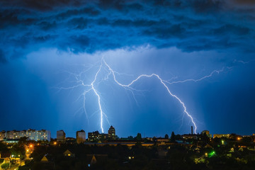 Naklejka na ściany i meble Lightning over the city in the night sky strikes the roof of the house