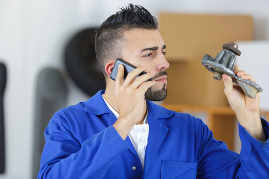 mechanic holding part calling factory on the phone