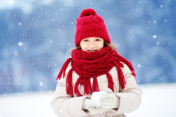 Adorable little girl having fun in beautiful winter park. Cute child playing in a snow.