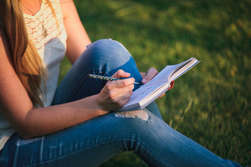 Girl copywriter sitting on the grass with notebook and pen. Woman freelancer writing outdoors.