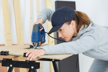 female carpenter cutting wood with an electrical jigsaw