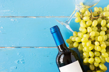 Bunches of fresh ripe white grapes and a bottle of wine on a blue wooden textural surface. space...