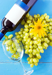 Bunches of fresh ripe white grapes and a bottle of wine on a blue wooden textural surface. space for advertising text