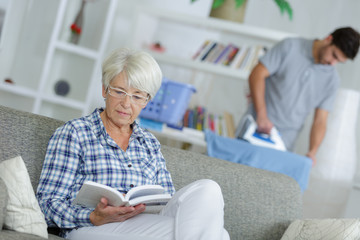 Obraz premium home help man ironing and senior lady reading a book