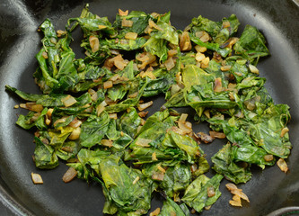 close up of sauteed collard greens with chopped shallot in cast iron frying pan skillet