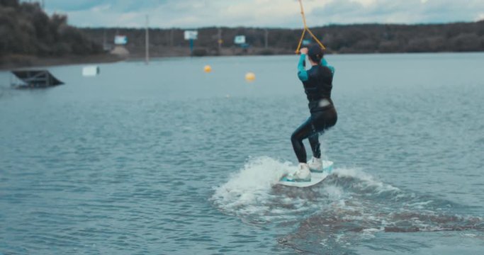 Attractive female wake boarding in a wakepark near a city. 4K UHD 60 FPS 