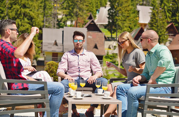 Beautiful stylish friends are using a digital tablet, drinking coffee and smiling while resting in the park
