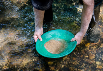 Gold pan filled with mineral rich material ready to be panned. Prospecting for gold and gemstones. Fun and adventure enjoying recreational outdoor activity.