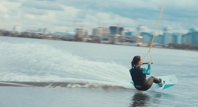Attractive female wake boarding in a wakepark near a city. 4K UHD 60 FPS 