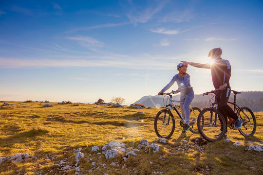 Biker couple with mountain bike pointing in distance at countryside