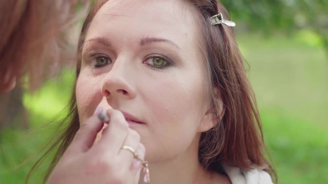 Make up artist applies lipstick on girl's lips before photoshoot