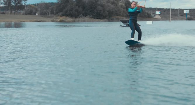 Attractive female wake boarding in a wakepark near a city. 4K UHD 60 FPS 
