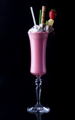Pink cocktail drink with strawberry, wafer tubule, candies on black background. Space in background for copy, text, your words	