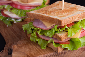 Close-up big sandwich with ham, cheese, tomatoes and salad on toasted bread on a dark background
