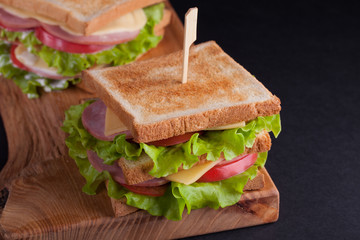 Close-up big sandwich with ham, cheese, tomatoes and salad on toasted bread on a dark background